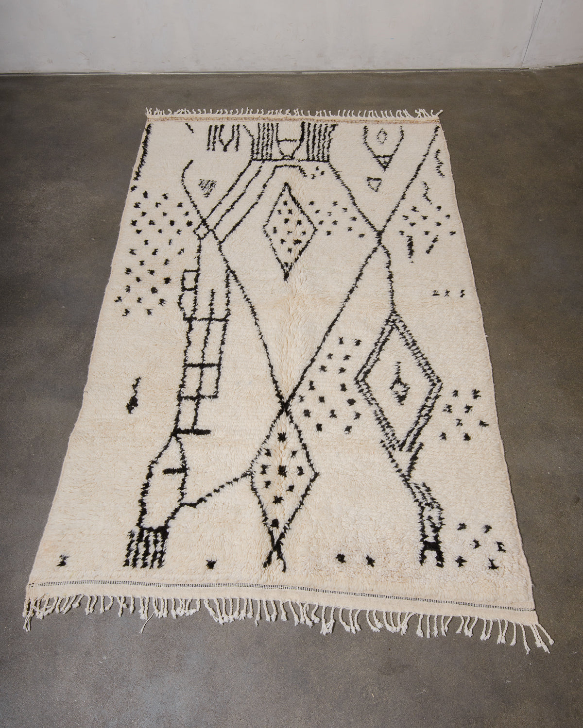 Azilal rug made of fluffy cream wool and black design laying on grey concrete floor